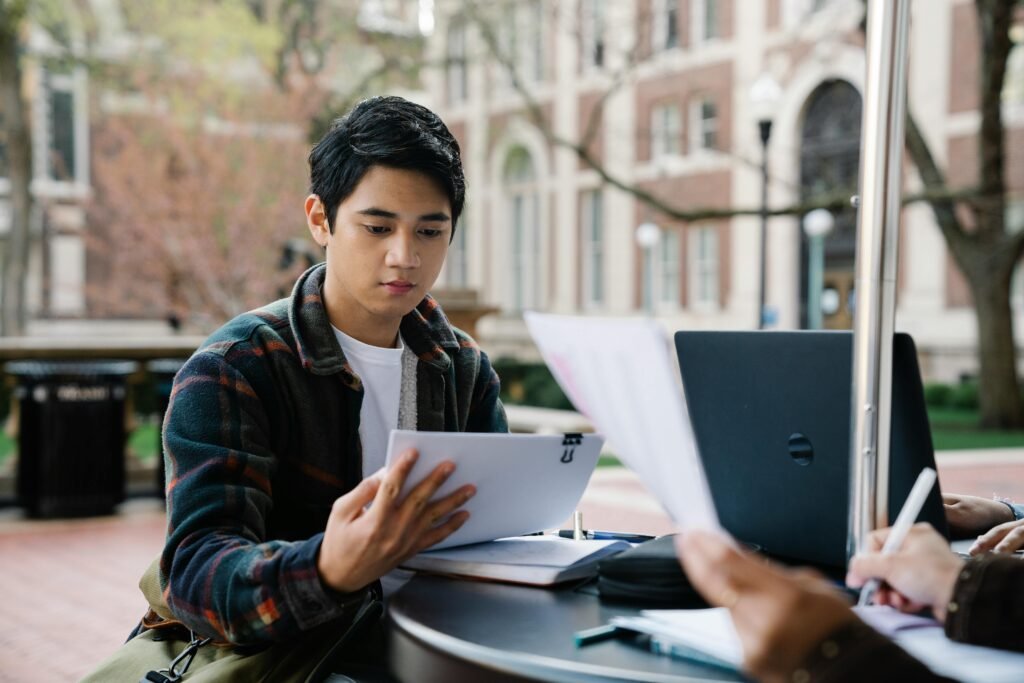 A college student reviews papers outside on campus with classmates, engaging in collaborative study.
